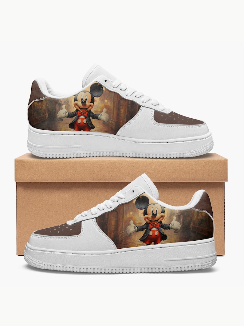 May include: A pair of white low-top sneakers featuring a brown toe box with perforated details and a side panel graphic of a cartoon mouse wearing a black tuxedo, red bowtie, and red shorts, standing in a dimly lit, warm-toned indoor setting.