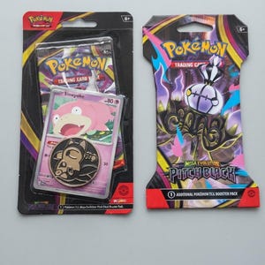 May include: Two Pokémon trading card blister packs. The left pack contains a pink Slowpoke card and a black and gold metal coin. The right pack features a purple and black Chandelure graphic with the text Mega Evolution Pitch Black.