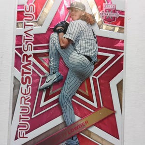 May include: A rectangular baseball trading card featuring Rhett Lowder in a pinstriped uniform, captured in a pitching motion. The background displays a large pink star design with the text FUTURE STAR STATUS and ELITE EXTRA EDITION.