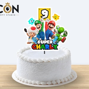Puede incluir: Un pastel con glaseado blanco decorado con un adorno de Super Mario que incluye a Mario, Luigi, Toad y Yoshi. El adorno presenta un bloque amarillo con el número 9 y el texto Super Charly en letras coloridas, gruesas y de estilo bloque.