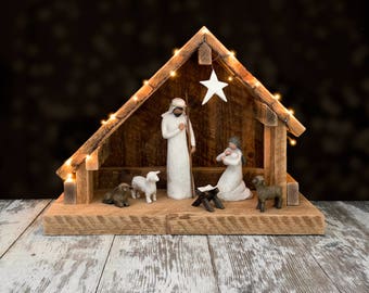 May include: A wooden nativity scene with a white star on the roof, a white figure of Joseph holding a staff, a white figure of Mary holding a baby, and two white lambs. The scene is lit with small white lights.