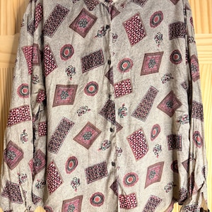 May include: A long-sleeved button-down shirt in a light beige color featuring an all-over pattern of dark red and black geometric shapes, including rectangles, diamonds, and circles, with small floral accents throughout the fabric design.