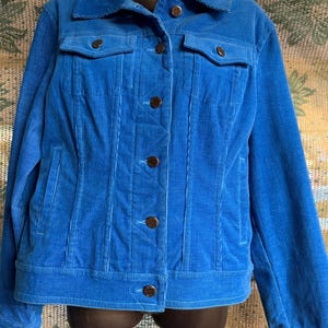 May include: A bright blue corduroy jacket with a classic design. The jacket features a collared neckline, two chest pockets, and four brown buttons down the front. The jacket has long sleeves and a tailored fit.