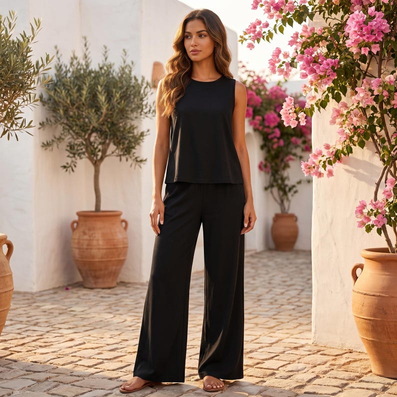 Puede incluir: Un conjunto negro liso compuesto por una blusa sin mangas con cuello redondo y pantalones de pierna ancha. El atuendo presenta una silueta relajada y fluida que llega hasta los tobillos, creando un estilo monocrom&aacute;tico y uniforme.
