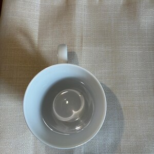 May include: A plain white ceramic mug viewed from directly above, showing a smooth, circular interior basin and a single curved handle extending from the side. The mug has a clean, minimalist design with a glossy finish and no patterns or text.
