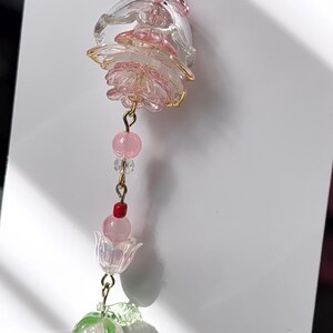 May include: A decorative charm featuring a clear and pink layered flower bead, a small pink bead, a tiny clear bead, a red bead, a second pink bead, a translucent tulip-shaped bead, and a light pink strawberry bead with green leaves.