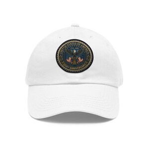 Puede incluir: Una gorra de béisbol blanca con un parche circular en la parte delantera. El parche muestra un águila calva, la Campana de la Libertad y banderas estadounidenses con el texto UNITED STATES OF AMERICA 1776-2026 250th ANNIVERSARY en letras doradas.