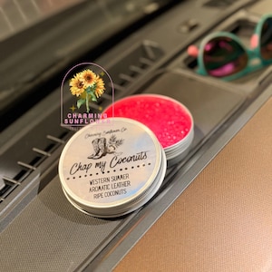 May include: Two small, round metal tins. One tin is filled with bright pink granules. The other tin has a label that reads "Chop my Coconuts" with "Western Summer, Aromatic Leather, Ripe Coconuts" below. A sunflower logo is in the background.