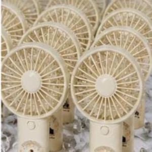 May include: A collection of cream-colored portable fans with a circular fan blade design. Each fan has a cylindrical base with a small image of a person. The fans are arranged on a white surface.