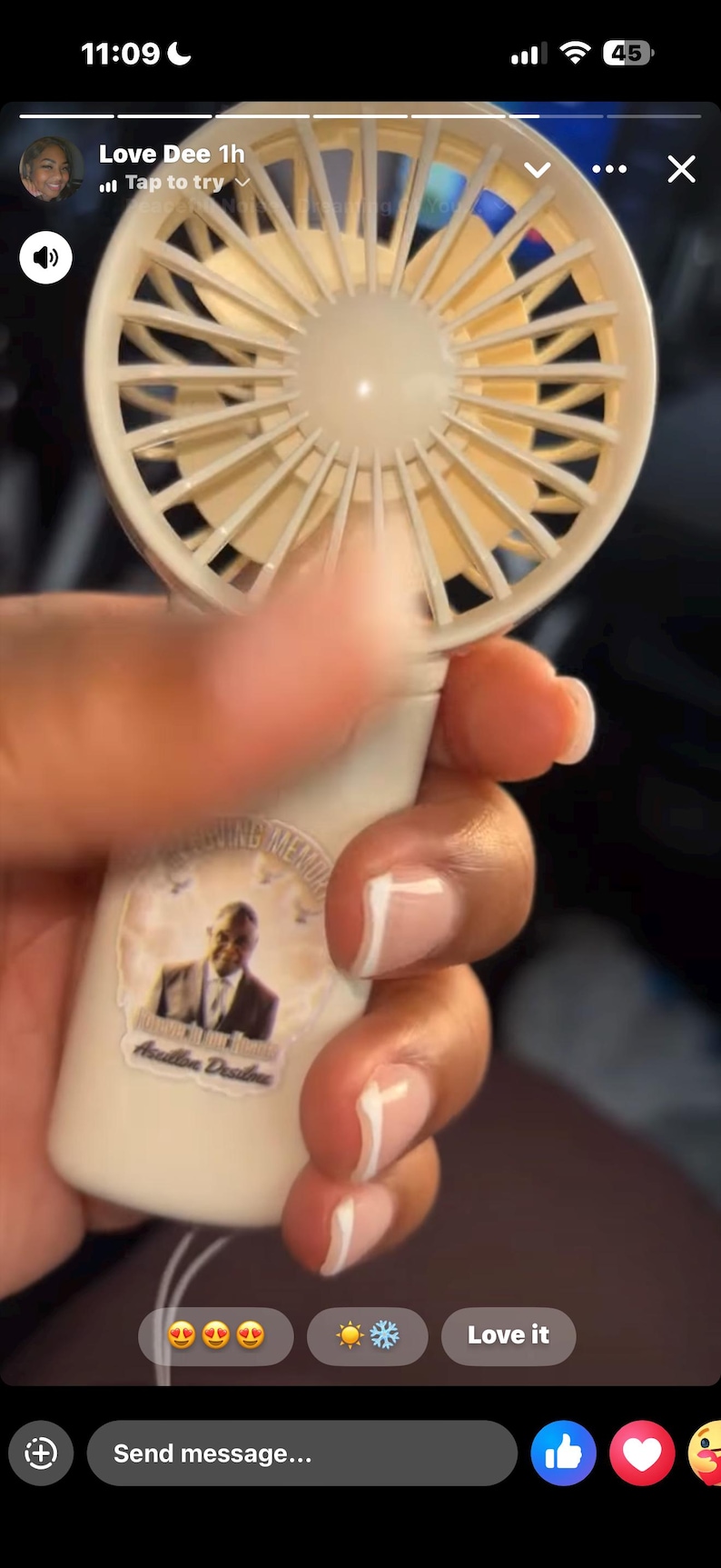 May include: A white and beige portable fan is held in a hand. The fan has a sticker with a photo and text. The fan is battery-operated and designed for personal cooling.