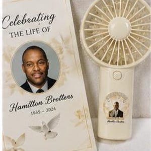 May include: A cream-colored handheld fan and a memorial card. The card reads "Celebrating The Life Of Hamilton Brottens 1965-2024" with a photo and dove graphic. The fan has a matching photo and is off-white.