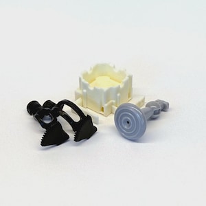 May include: A collection of small plastic construction toy components including a white square castle-like turret piece, two black articulated claw-like parts with serrated edges, and a single gray circular stand with a central pin and connector.