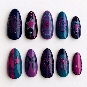 May include: A set of ten almond-shaped press-on nails featuring a dark color palette of navy, purple, and teal. The designs include raised 3D-style accents such as hearts, stars, bows, spiderwebs, and swirling patterns with glossy finishes.