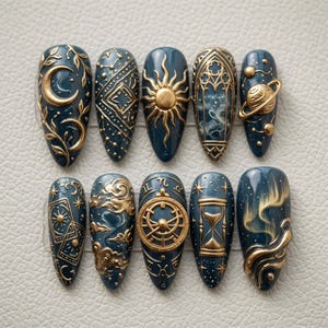 May include: A set of ten almond-shaped press-on nails in a deep navy blue base color. Each nail features intricate, raised gold-toned relief designs including a crescent moon, sun, Saturn-like planet, tarot cards, a compass, and an hourglass.