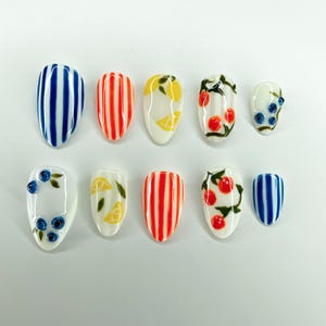 May include: A set of ten press-on nails featuring various designs including blue and white vertical stripes, orange and white vertical stripes, yellow lemon slices with green leaves, red cherries with green stems, and blue blueberries with green leaves.