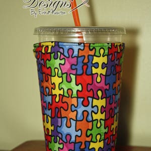 May include: A colorful puzzle piece patterned fabric cup cozy for a cold beverage. The cozy is made of a soft, washable fabric and is designed to fit most standard-sized cups.