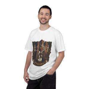 May include: A white short-sleeved t-shirt featuring a graphic illustration of a person in traditional attire holding a smoking incense burner in front of stone structures, with the word ETHIOPIA printed in a banner at the bottom of the design.