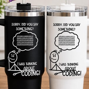May include: Two stainless steel tumblers with handles and straws, one black and one white. Both feature a stick figure graphic, a thought bubble containing binary code, and the text: SORRY, DID YOU SAY SOMETHING? I WAS THINKING ABOUT CODING!