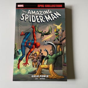 Può includere: Un libro tascabile Marvel Epic Collection intitolato The Amazing Spider-Man: Great Power di Lee e Ditko. La copertina presenta un'illustrazione colorata di Spider-Man in un costume rosso e blu che combatte vari cattivi tra cui il Dottor Octopus.