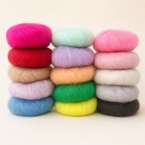 Può includere: Una collezione di quindici gomitoli di filato soffice impilati in tre colonne verticali. I colori includono rosa vivace, rosso, beige, viola chiaro, blu, verde menta, lavanda, arancione, verde brillante, giallo, rosa tenue, bianco, grigio e marrone scuro.