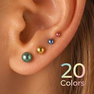 May include: Four spherical stud earrings in varying sizes and colors, including metallic green, gold, blue, and pink, are worn in a row along the earlobe and cartilage. The text 20 Colors is displayed in the lower right corner in a gradient font.