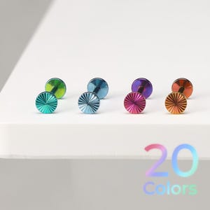 May include: Four labret studs with flat backs and circular fronts featuring a sunburst or radial line pattern. The studs are finished in iridescent metallic colors including green, blue, purple, and orange. The text 20 Colors is visible.