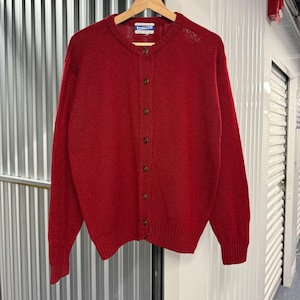 May include: A solid red long-sleeve cardigan sweater featuring a crew neckline, a front button-down closure with brown buttons, and ribbed cuffs and hem. A Pendleton brand label is stitched inside the collar of this knit garment.
