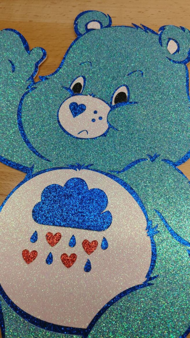 May include: A blue glitter Care Bear with a white belly and a blue cloud with red hearts raining from it.