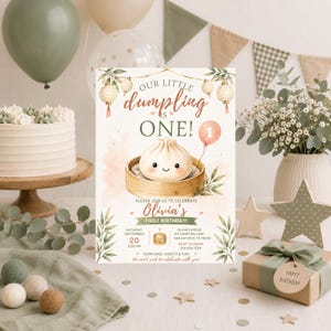 Könnte beinhalten: Eine Geburtstagseinladungskarte mit einem niedlichen illustrierten Dumpling im Bambusdämpfer, hängenden Papierlaternen und einem rosa Ballon mit der Zahl Eins. Der Text lautet Our Little Dumpling Is One, Olivia's First Birthday und Veranstaltungsdetails.