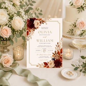 Puede incluir: Una tarjeta de invitación de boda rectangular con fondo crema, borde dorado e ilustraciones florales en burdeos, óxido y beige. El texto dice Olivia Reynolds y William Thompson, sábado 25 de octubre de 2027, a las 17:00 horas.
