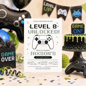 May include: A white rectangular birthday invitation card featuring a black pixelated video game controller graphic, the text "LEVEL 8 UNLOCKED!", "JAXSON'S 8TH BIRTHDAY!", and event details including date, time, location, and RSVP information in black and green.