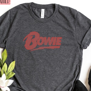 May include: Dark grey heather t-shirt with the word "BOWIE" printed in red on the front.