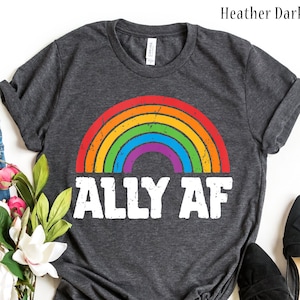 May include: Heather dark grey t-shirt with a rainbow design and the text "ALLY AF" in white. The rainbow features red, orange, yellow, green, blue, and purple colors. The shirt is a casual wear item.