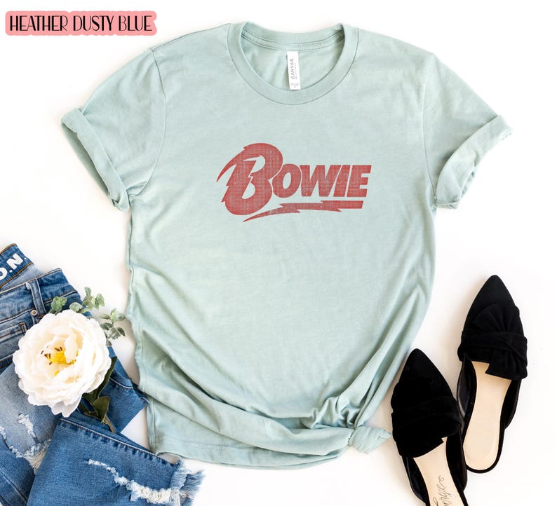 May include: A heather dusty blue t-shirt with a red vintage-style graphic of the word "BOWIE" on the front.