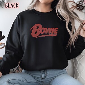 May include: Black sweatshirt with a red "BOWIE" graphic on the front.