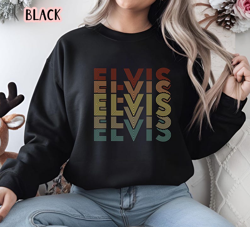 Puede incluir: Sudadera negra con un gr&aacute;fico de estilo retro de la palabra "Elvis" repetida en diferentes colores y fuentes.
