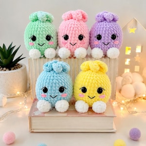 Puede incluir: Cinco pequeños peluches redondos de ganchillo en colores pastel: verde menta, rosa, lavanda, azul claro y amarillo. Cada peluche tiene una superficie de hilo texturizado, dos ojos de plástico negro, una boca negra bordada, mejillas rosas y dos pequeños pies blancos.
