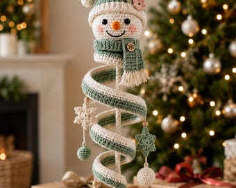 Puede incluir: Un adorno de muñeco de nieve tejido a ganchillo con un gorro verde salvia con una pequeña flor rosa, una bufanda a juego con un botón de madera y un cuerpo largo en espiral. La espiral está decorada con copos de nieve, esferas y una borla.