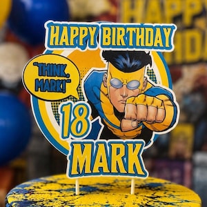 May include: A circular cake topper featuring a comic book character in a yellow and blue suit with a speech bubble that says THINK, MARK! The topper includes the text HAPPY BIRTHDAY, the number 18, and the name MARK in bold blue and yellow letters.