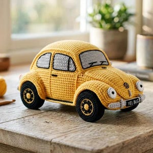 May include: A yellow crocheted toy car shaped like a classic beetle, featuring grey windows, black tires with yellow centers, and a front license plate that reads YEL BUG. The car has round headlights and a small black emblem on the hood.