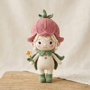 May include: A handmade crochet doll in the shape of a flower fairy. The doll has a pink flower-shaped hat, green cape, and boots. It holds a yellow flower. The doll is approximately 6 inches tall.