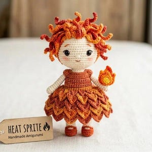 May include: A crochet amigurumi doll with curly orange and red hair, wearing a layered orange and brown leaf-patterned dress and matching shoes. The doll holds a small flame-shaped object and stands next to a wooden tag labelled HEAT SPRITE.