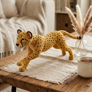 May include: A handcrafted crochet cheetah figurine in a dynamic running pose. The toy features a golden-yellow yarn body with black spots, a white underbelly, black facial markings, and small ears with pink inner details, standing on four legs.