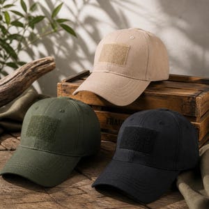May include: Three baseball caps in beige, olive green, and black. Each cap features a structured crown, a curved brim with stitched detailing, and a rectangular hook-and-loop fastener patch on the front panel for attaching patches or insignias.