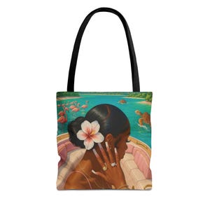 Peut inclure: Un sac fourre-tout à anses noires orné d'une illustration représentant une personne avec une fleur blanche dans les cheveux, assise dans un bateau sur une eau turquoise. La scène montre des flamants roses près d'une plage et une tortue marine.