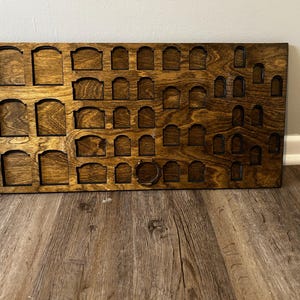 May include: A rectangular dark brown wooden display board featuring a grid of various sized recessed arch-shaped slots. The board has a smooth, stained finish with visible wood grain patterns throughout the surface, designed for organizing small items.