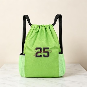 May include: A bright lime green drawstring backpack made of a textured mesh material. The bag features black shoulder straps and two side mesh pockets. Centered on the front is the number 25 in a bold black font with a thin white outline.