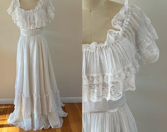 Puede incluir: Un vestido blanco largo hasta el suelo con corpiño y falda plisados, un escote ancho con volantes y encaje, y mangas cortas con volantes. La cintura está definida por una banda lisa y la falda incluye un dobladillo con volantes escalonados.
