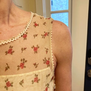 May include: A white sleeveless dress with a floral pattern and a lace trim. The dress has a zipper on the back.
