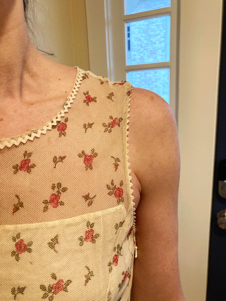May include: A white sleeveless dress with a floral pattern and a lace trim. The dress has a zipper on the back.